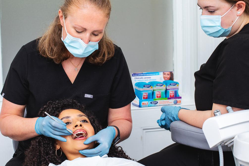 Dentist inspecting inside a patients mouth with a dental mirror. Dental nurse looking on.